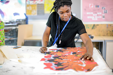 A young woman in a bright textile studio spreads out a beautifully screen-printed African patterned fabric