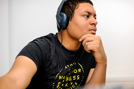 A young man listens to music on his headphones while working on an assignment