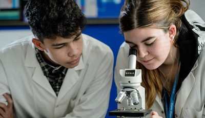 Two students in lab coats looking down a microscope